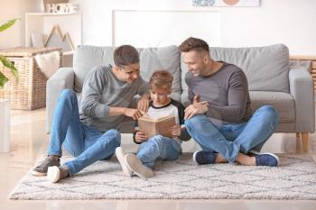 Happy gay couple with adopted child reading book at home�