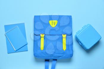 School backpack, lunchbox and notebooks on color background�