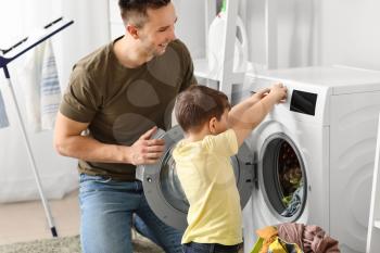 Man and his little son doing laundry at home�