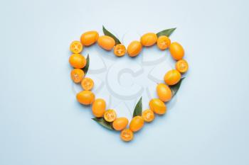 Heart made of tasty kumquat fruit on color background�