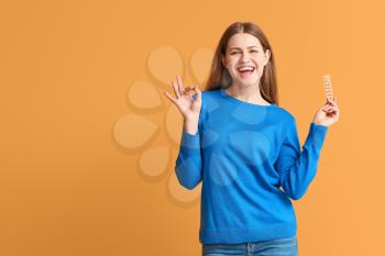 Young woman with birth control pills showing OK on color background�