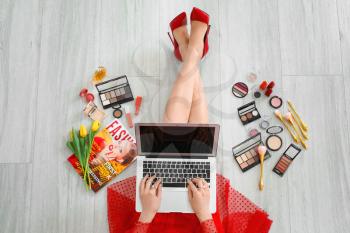 Female makeup artist with laptop and cosmetics at home�