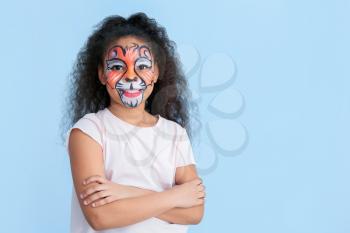 Funny African-American girl with face painting on color background�