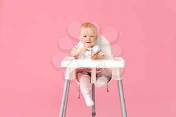 Cute little baby sitting in high-chair on color background�