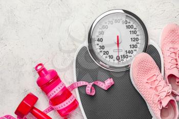 Weight scales with measuring tape, sport shoes, dumbbell and bottle of water on light background�