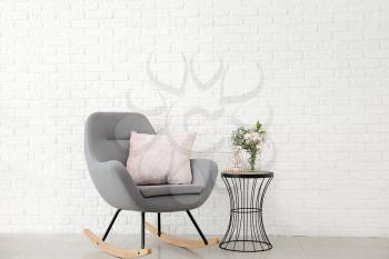 Interior of modern room with comfortable armchair and table with spring flowers near brick wall�