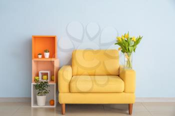 Interior of modern room with comfortable armchair, shelf unit and spring flowers near light wall�