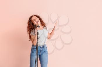 Young African-American woman singing on color background�