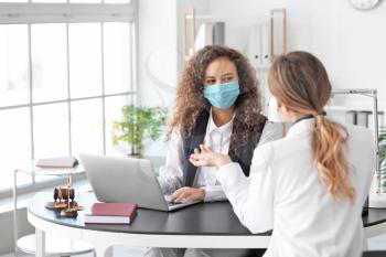 Female lawyer in protective mask working with client in office�
