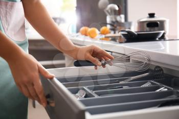 Woman putting whisk into kitchen drawer�