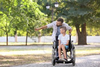 Teenage boy in wheelchair with his father outdoors�