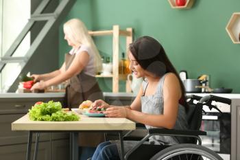 Young woman in wheelchair eating at home�