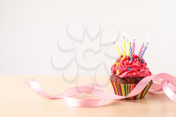 Delicious birthday cupcake with burning candles and ribbon on light wooden table�