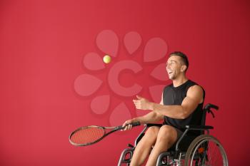 Young tennis player sitting in wheelchair on color background�