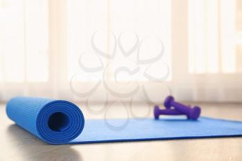 Yoga mat with dumbbells on light floor�