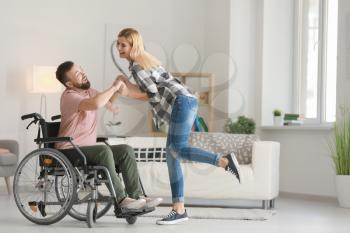 Man in wheelchair with beautiful woman dancing at home�