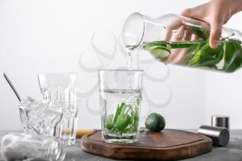 Woman pouring tasty fresh cucumber water from bottle into glass on light background�