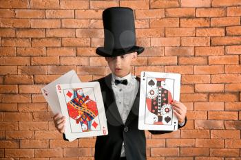 Cute little magician with cards against brick wall�
