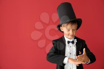 Cute little magician showing tricks on color background�