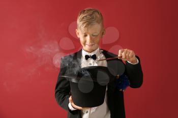 Cute little magician showing trick with hat on color background�
