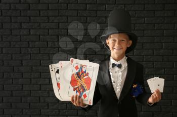 Cute little magician with cards against dark brick wall�