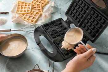 Woman pouring raw dough in modern waffle maker on light table�