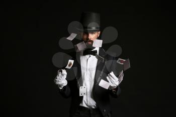 Magician showing tricks with cards on dark background�