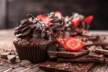 Tasty cupcakes with strawberry and pieces of chocolate bar on wooden table�