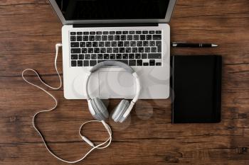 Headphones with laptop and notebook on wooden table�