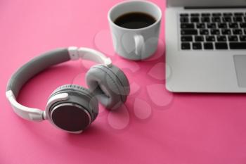 Headphones with laptop and cup of coffee on color table�