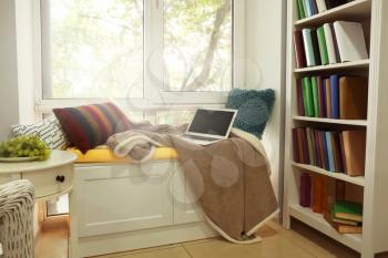 Cozy place for rest with soft pillows and laptop near window�