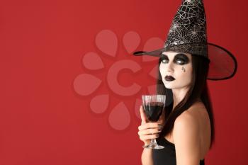 Beautiful woman dressed as witch for Halloween with wine on color background�