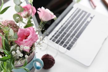 Vase with beautiful flowers and laptop on white table�