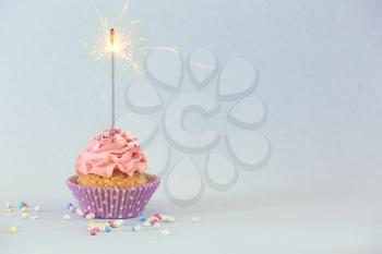 Delicious birthday cupcake with firework candle on color background�
