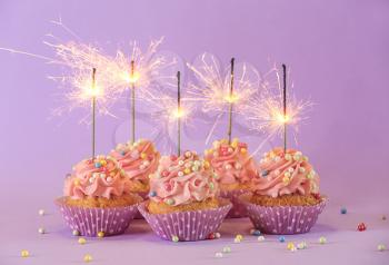 Delicious birthday cupcakes with firework candles on color background�