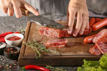 Woman cutting delicious smoked sausage on wooden board�