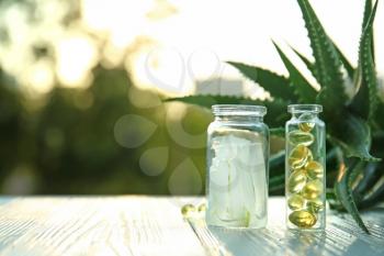 Bottles with peeled aloe vera and pills on table outdoors�