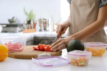 Woman cutting fresh pepper for freezing on wooden board in kitchen�