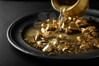 Pouring of water on plate with gold nuggets�
