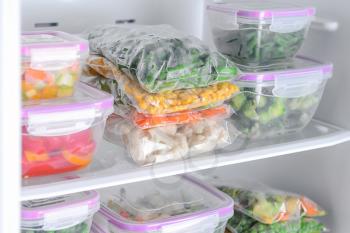 Containers and plastic bags with frozen vegetables in refrigerator�