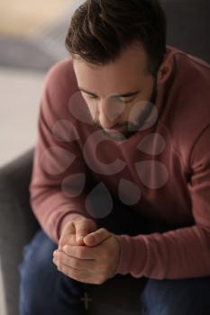 Religious young man praying to God at home�