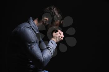Religious young man praying to God on black background�
