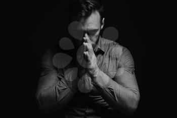 Religious young man praying to God on dark background, black and white effect�