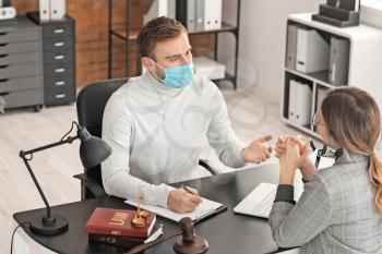Male lawyer in protective mask working with client in office�