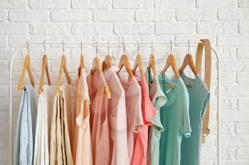 Rack with hanging clothes near brick wall�