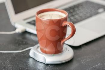 Cup of coffee with heater and laptop on table�