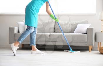 Young woman mopping floor in room�