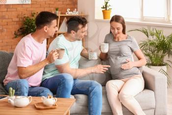 Gay couple with pregnant woman drinking tea at home�