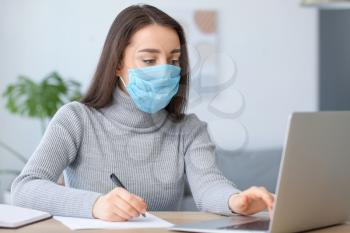 Young woman wearing medical mask while working in office�