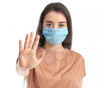 Young woman in medical mask showing STOP gesture against white background�